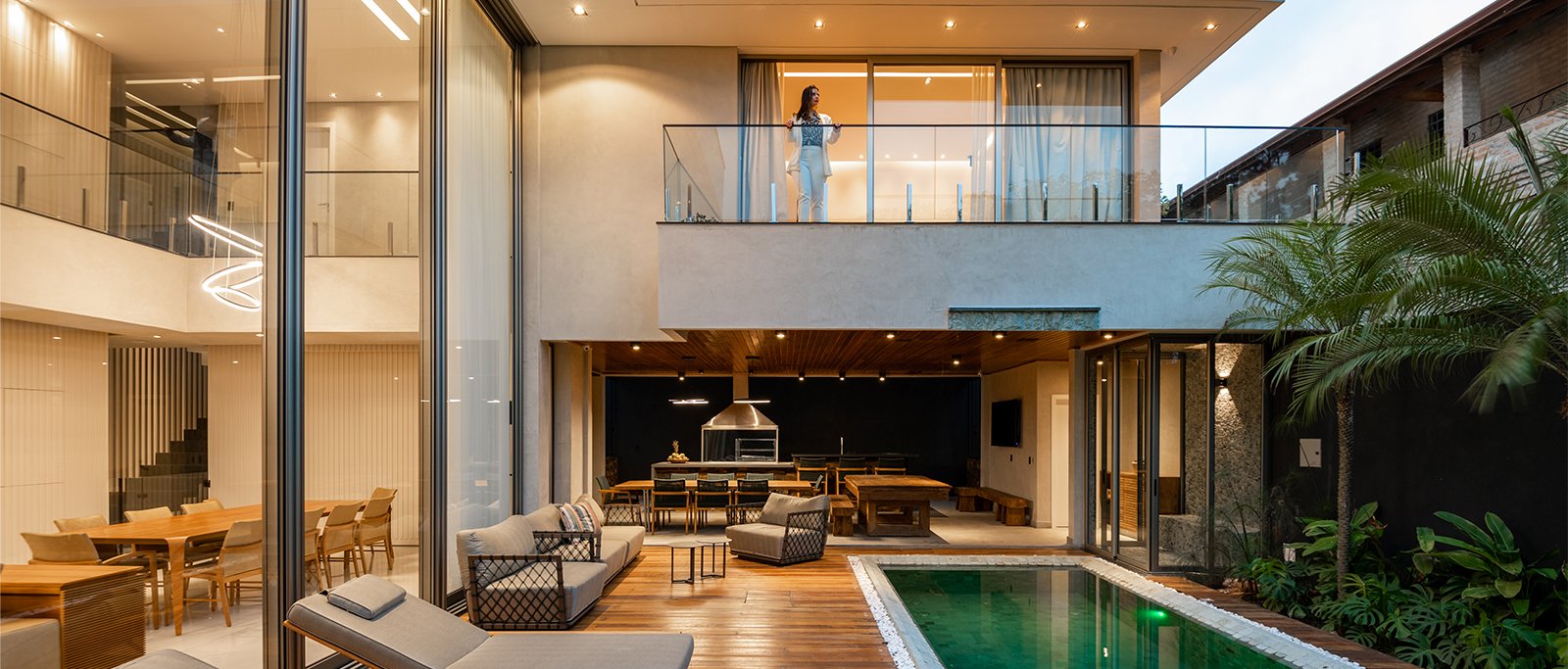 Área de lazer de luxo com piscina revestida em pedra verde e amplo deck de madeira. Fachada contemporânea de residência no Alto da Boa Vista projetada pela arquiteta Flavia Medina, mostrando integração entre área gourmet e interior envidraçado.